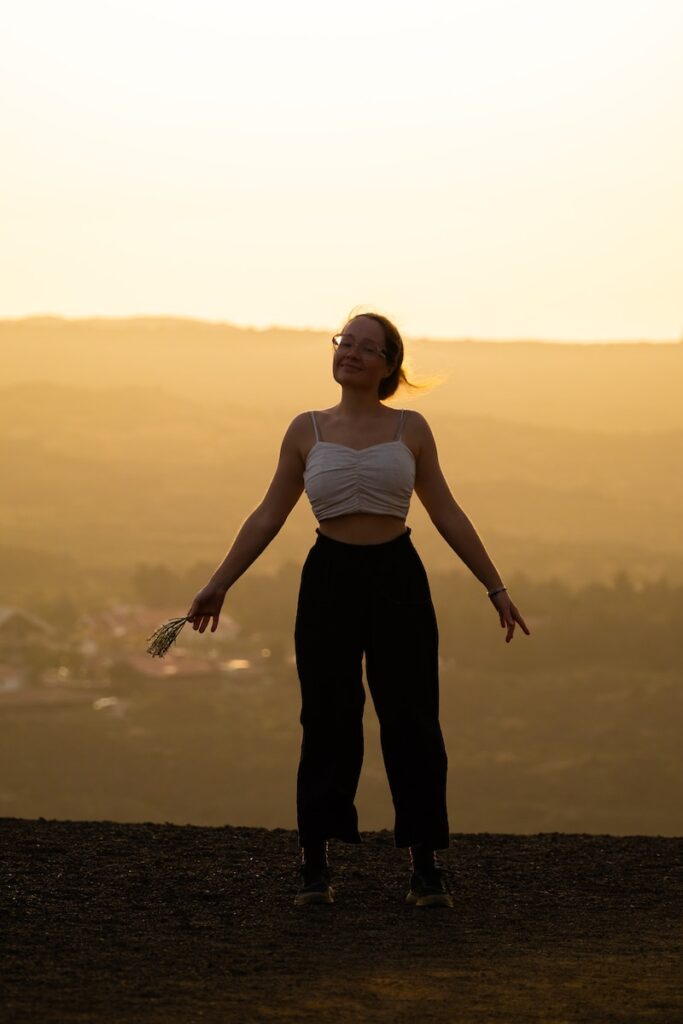 a woman standing on top of a hill with her arms outstretched, Feminization