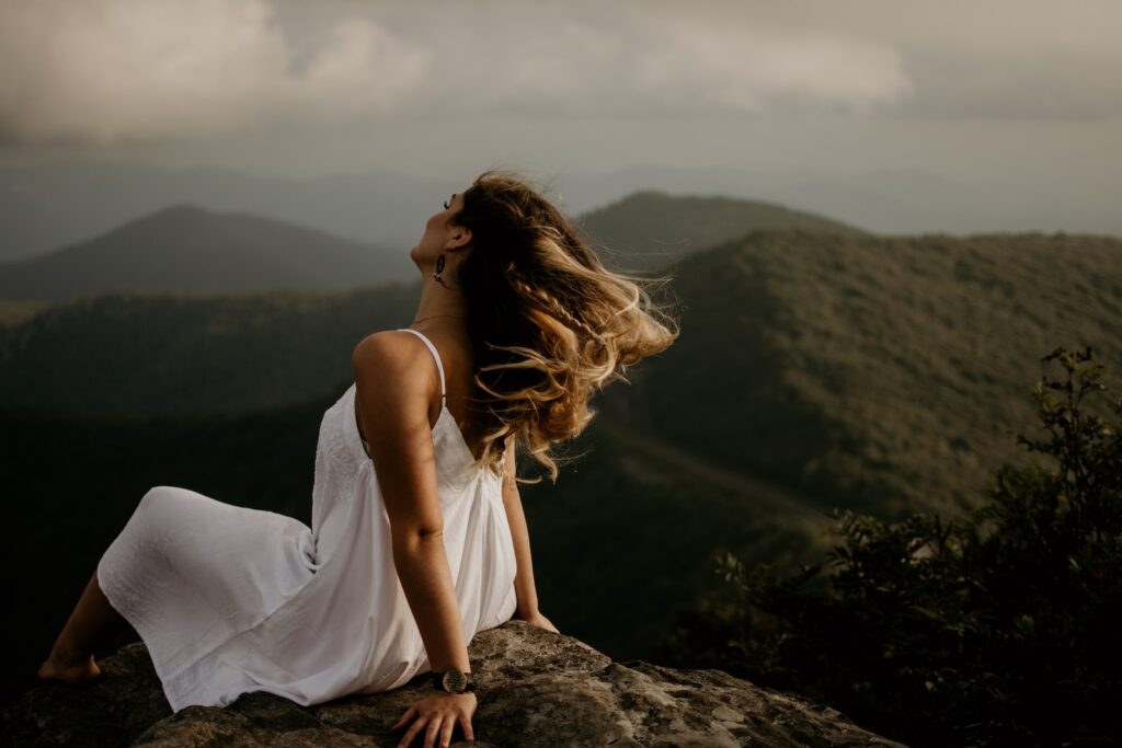 woman in white sleeveless dress sitting on hill, more feminine look