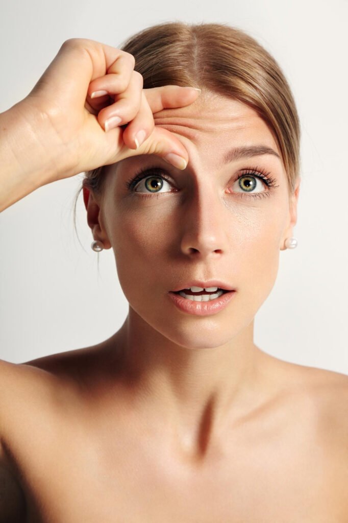 Voorhoofdverkleining bij Facial Feminization Surgery (FFS) 1 jonge schoonheidsvrouw vraagt zich af dat ze rimpels op haar voorhoofd heeft