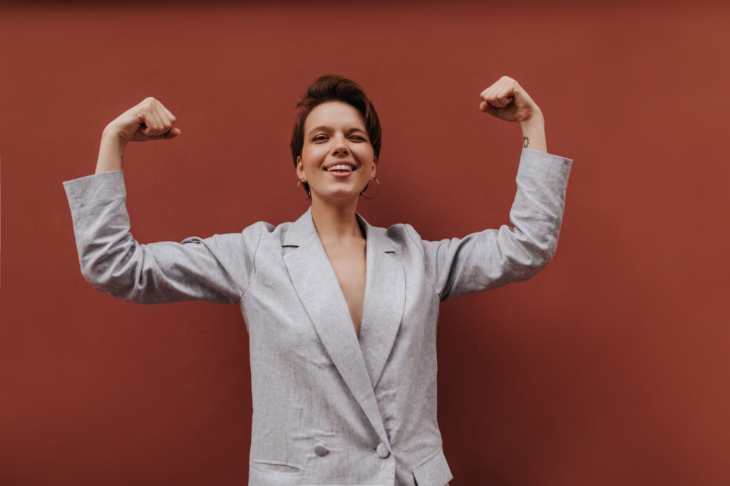pretty lady suit showing her biceps brown background short haired woman grey stylish jacket demonstrates power isolated